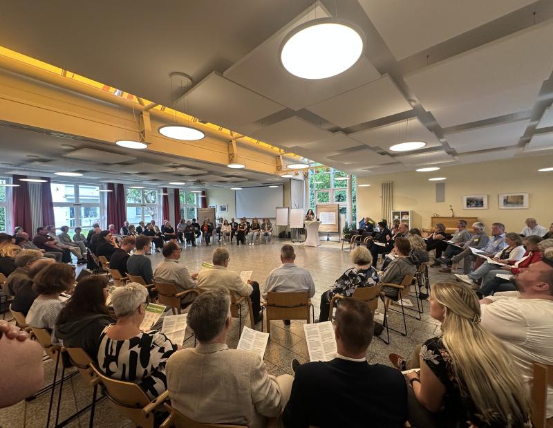 Kirche in Lippe - Wegweisende Beschlüsse: die Lippische Landessynode hat im Gemeindezentrum St. Pauli in Lemgo getagt. Ein großer Raum im Gemeindezentrum St. Pauli in Lemgo. Viele Leute sitzen in einem großen Stuhlkreis. Eine junge Frau steht und spricht.